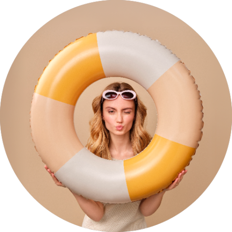 Frau mit langen blonden Haaren und Sonnenbrille, die ein Kussgesicht durch einen gelben und weißen aufblasbaren Schwimmring vor einem beigen Hintergrund macht.