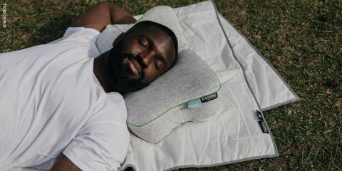 Eine Person in Sportkleidung schläft auf einem grauen Sofa mit einem weißen Kissen, die Arme verschränkt, im Hintergrund ein Fahrrad und darunter ein Parkettboden.