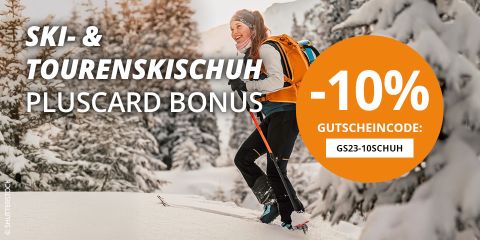 Nahaufnahme einer Person in Winterkleidung, die auf einem schneebedeckten Hang schwarze Skibindungen einstellt. Der Text auf dem Bild bietet mit einem Promo-Code mit Atomic-Branding 10 % Rabatt auf Skischuhe.