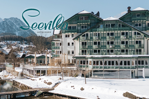Großes Hotel am See mit grüner Umrandung in verschneiter Winterlandschaft, Berge im Hintergrund, Person am Wasser stehend; "Seevilla"-Logo oben links.
