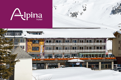 Verschneites Hotel Alpina mit Balkonen und dekorativer Fassade vor einer verschneiten Bergkulisse; lila Logo in der linken oberen Ecke.