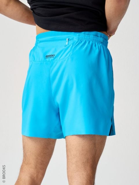 Person in hellblauen Sporthosen und einem schwarzen Oberteil, von hinten vor einem hellen Hintergrund fotografiert.