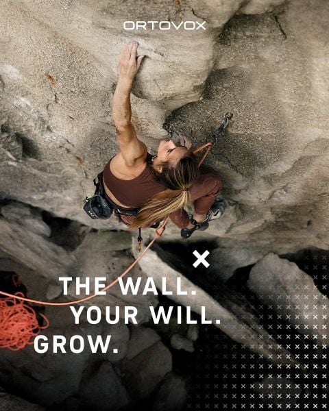 Eine Frau klettert eine steile Felswand hinauf, wobei sie sich mit einer Hand nach oben streckt. Der Text lautet: "DIE MAUER. DEIN WILLE. WACHSEN." Darüber befindet sich das Ortovox-Logo.