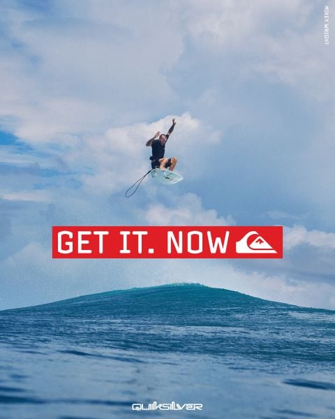 Ein Surfer springt unter blauem Himmel hoch über eine Welle. Der fettgedruckte rote Text lautet "GET IT. NOW", darunter das Quiksilver Logo.