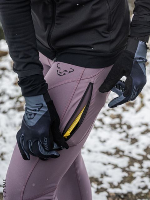 Zwei Personen, die nachts in Sportkleidung laufen, mit sichtbaren Regentropfen in der Luft und nassem Bürgersteig unter ihnen. Beide Läufer tragen Jacken und Laufschuhe und laufen schnell an einem Metalltor vorbei.