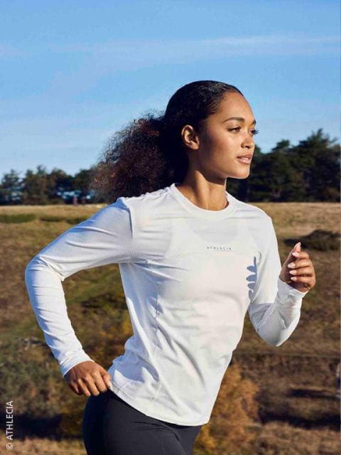 Vier Personen in Winterlaufkleidung joggen gemeinsam auf einem verschneiten Weg unter einer Betonbrücke, lächeln und genießen die Bewegung im Freien.